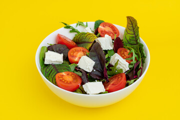 fresh Greek salad in white bowl isolated on yellow background