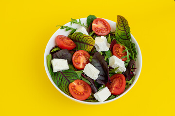 fresh Greek salad in white bowl isolated on yellow background