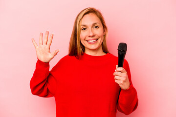 Young caucasian singer woman isolated on pink background smiling cheerful showing number five with fingers.