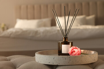 Aromatic reed air freshener and flower on bench in bedroom, space for text