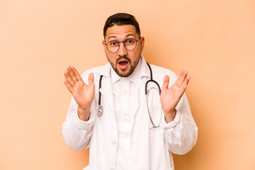 Hispanic doctor man isolated on beige background surprised and shocked.