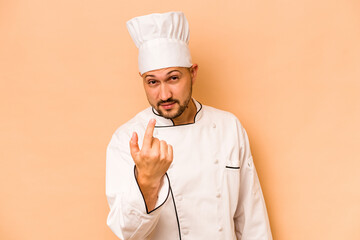 Hispanic chef man isolated on beige background pointing with finger at you as if inviting come closer.