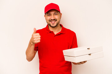 Young delivery man holding pizzas isolated on beige background smiling and raising thumb up