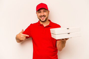Young delivery man holding pizzas isolated on beige background person pointing by hand to a shirt copy space, proud and confident