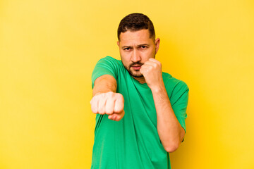 Young hispanic man isolated on yellow background throwing a punch, anger, fighting due to an argument, boxing.