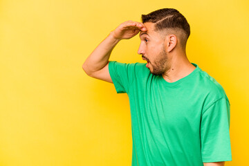 Young hispanic man isolated on yellow background looking far away keeping hand on forehead.