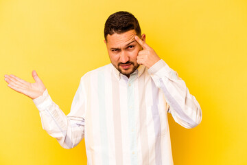 Young hispanic man isolated on yellow background showing a disappointment gesture with forefinger.