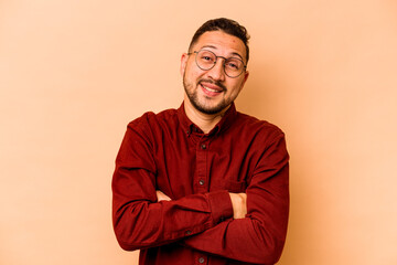 Young hispanic man isolated on beige background who feels confident, crossing arms with determination.