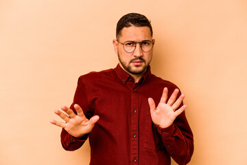 Young hispanic man isolated on beige background rejecting someone showing a gesture of disgust.