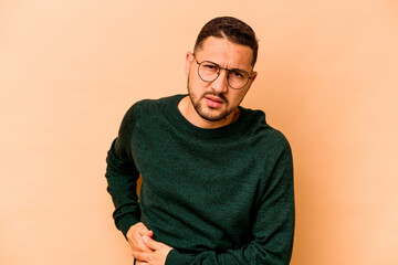 Young hispanic man isolated on beige background having a liver pain, stomach ache.