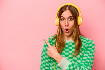 Young caucasian woman listening to music isolated on pink background pointing to the side