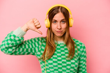 Young caucasian woman listening to music isolated on pink background showing a dislike gesture,...