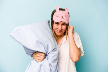 Young caucasian woman wearing a pajama isolated on blue background covering ears with hands.