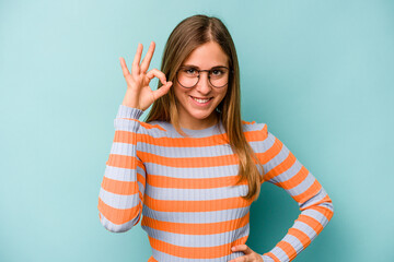 Young caucasian woman isolated on blue background cheerful and confident showing ok gesture.