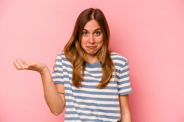 Young caucasian woman isolated on pink background doubting and shrugging shoulders in questioning...