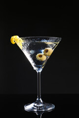 Martini cocktail with olives and lemon twist on dark background