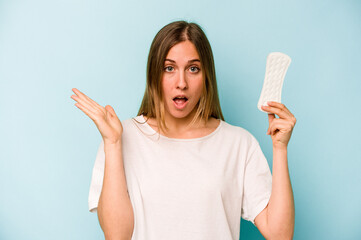 Young caucasian woman holding sanitary napkin isolated on blue background surprised and shocked.