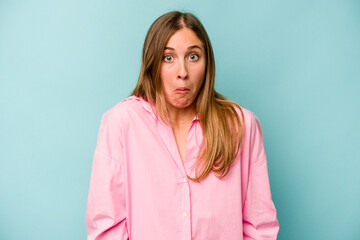 Young caucasian woman isolated on blue background shrugs shoulders and open eyes confused.