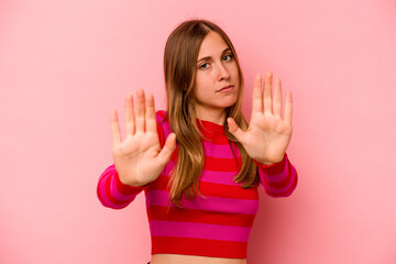 Young caucasian woman isolated on pink background standing with outstretched hand showing stop sign, preventing you. - obrazy, fototapety, plakaty