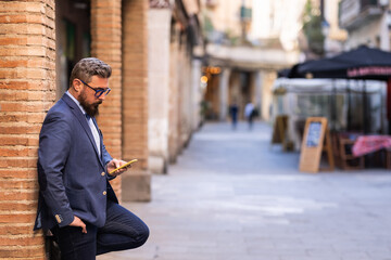 Businessman using a mobile phone while leaning on a column outdoors in the street.