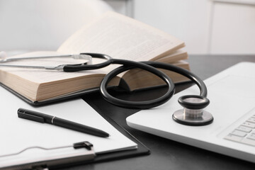 Open student textbook, clipboard and stethoscope near laptop on grey table indoors, closeup....