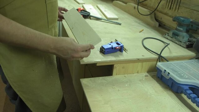 A mature carpenter makes a shelf in his carpentry workshop, works with a tool with wood