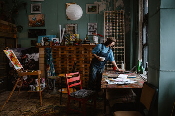 Young woman artist using laptop while working in her studio - obrazy, fototapety, plakaty