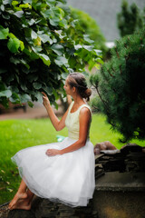 Pretty woman girl in a skirt is sitting near a small pond in a beautiful garden. Garden art and a beautiful classic lawn garden