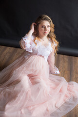 Young cute pregnant woman with long red hair in a delicate airy dress with lace on a black background. Happy motherhood. Mothers Day