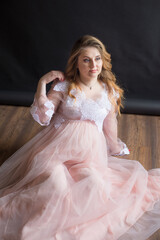 Young cute pregnant woman with long red hair in a delicate airy dress with lace on a black background. Happy motherhood. Mothers Day