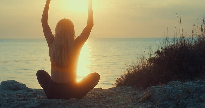 Young women are doing yoga in summer sunset with sea background. Warm-up, healthy life, relaxing and outdoor exercise. Health care, authenticity, sense of balance and calmness.
