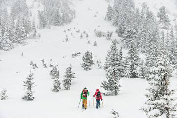 Two male skiers in bright suits with ski equipment are walking along the winter snow trail