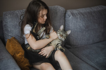 Dziecko tulące kota na szarej kanapie - obrazy, fototapety, plakaty