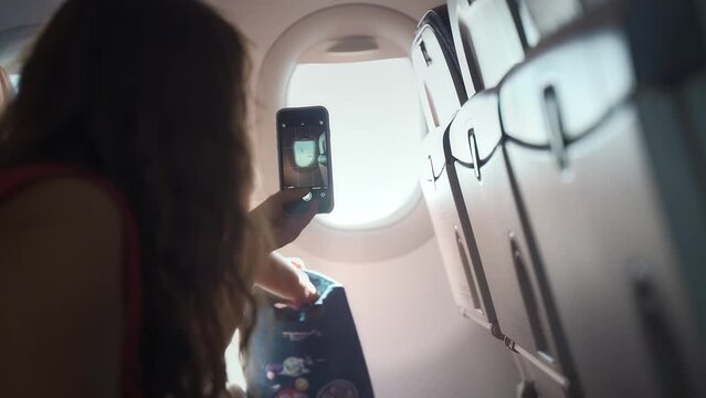 woman takes a picture of the view from the airplane window on her phone. Traveling by plane with children.