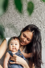Portrait of happy mother with little daughter in bedroom closeup, blurred background. Hold in hands and have fun with baby, capture happy emotions. Concept of maternal affection and childcare.