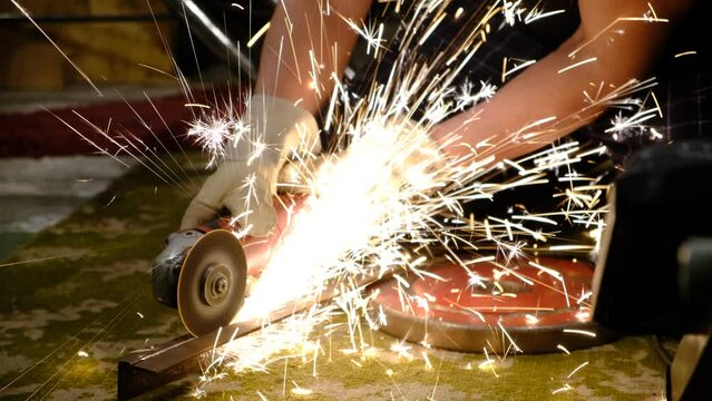 man worker at home cuts metal with a grinder. Hands in work gloves, Many luminous sparks from the operation of an electronic device. Metal processing and cutting. locksmith work