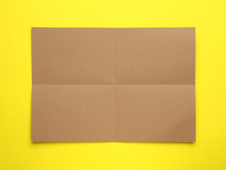 Fototapeta premium Sheet of brown paper on yellow background, top view