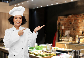 cooking, advertisement and people concept - happy smiling female chef in white toque and jacket holding something on palm of her hand over restaurant kitchen background
