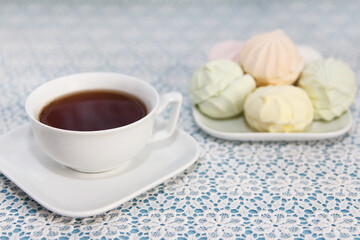 Traditional delicious brewed tea in a cup and air marshmallows lie on table