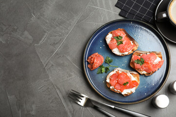 Tasty bruschettas with salmon, cream cheese and parsley on grey table, flat lay. Space for text