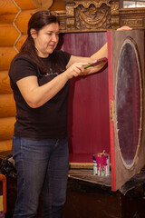 Woman with brush looking at door of antique cupboard with beautiful ornaments and painting it....