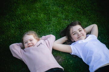 Dwie dziewczynki leżą obok siebie na plecach na zielonej trawie - obrazy, fototapety, plakaty