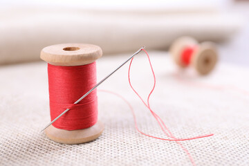 Spool of red sewing thread with needle on white fabric, closeup