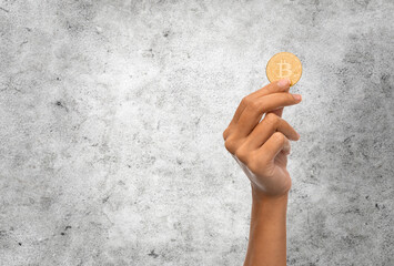 cryptocurrency, finance and business concept - close up of female hand holding golden bitcoin over grey stone wall background