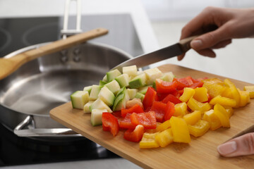 Woman putting cut vegetables into saute pan in kitchen, closeup - obrazy, fototapety, plakaty