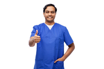 healthcare, profession and medicine concept - happy smiling indian doctor or male nurse in blue uniform showing thumbs up over white background