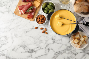 Pot of tasty cheese fondue and snacks on white marble table, flat lay. Space for text
