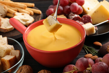 Dipping piece of bread into tasty cheese fondue at black table, closeup