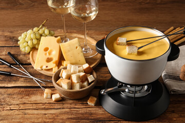 Pot of tasty cheese fondue, snacks and wine on wooden table