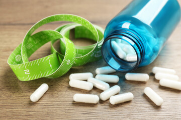 Jar of weight loss pills and measuring tape on wooden table, closeup